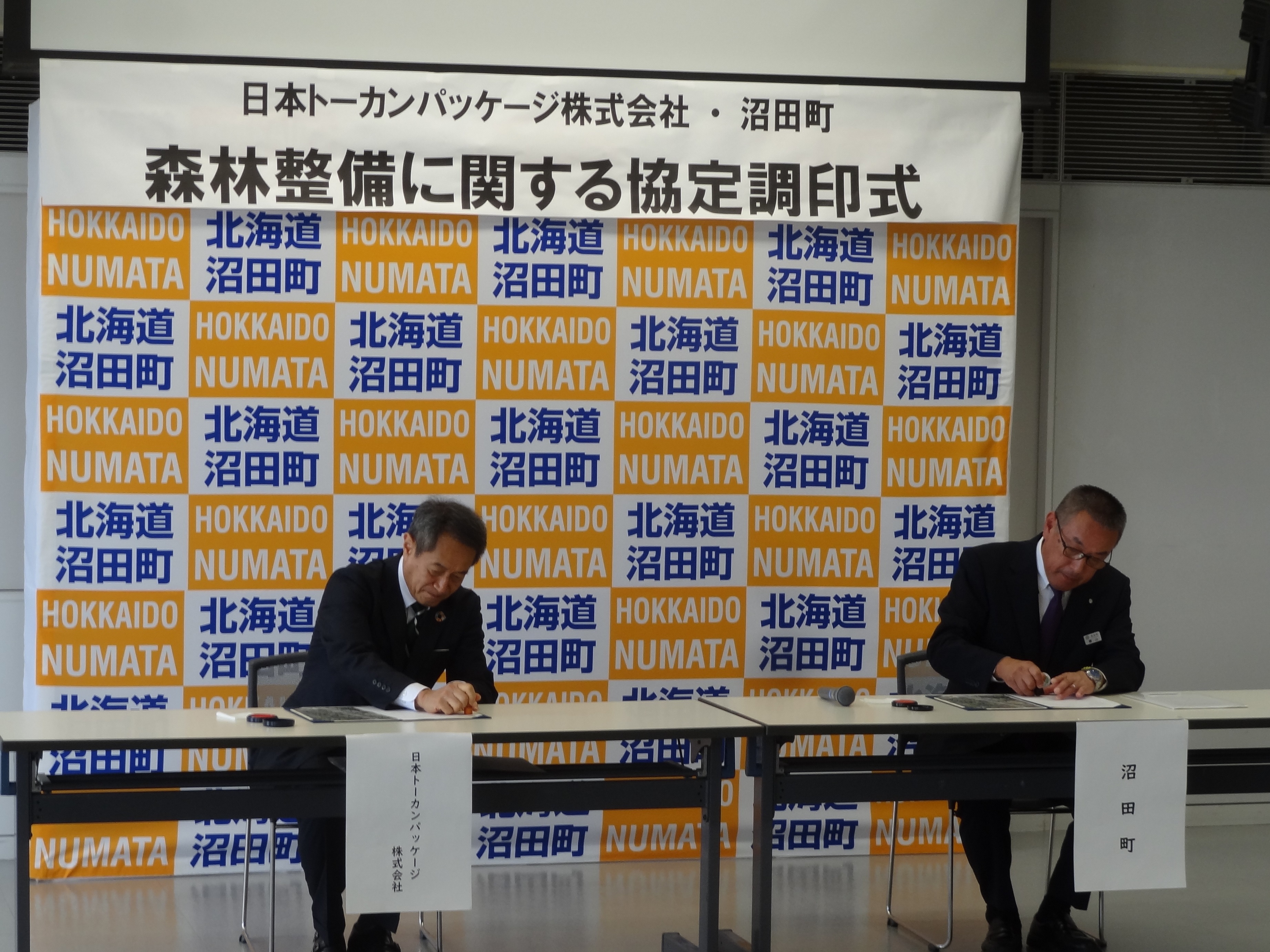 梶原専務（左）と横山町長（右）との間で、協定書の署名の取り交わしが行われました